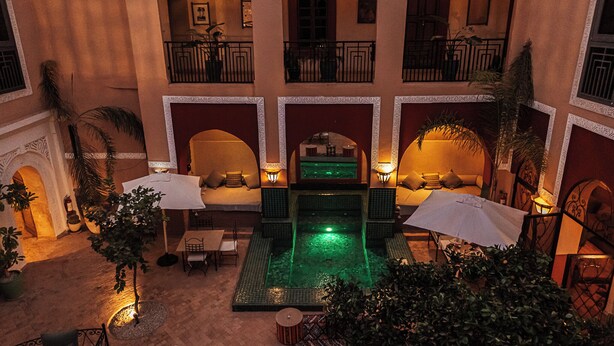 A multi-level hotel with a central courtyard featuring a pool, outdoor seating, and balconies. - Le Riad Medina Privilège & Spa (Marrakech)