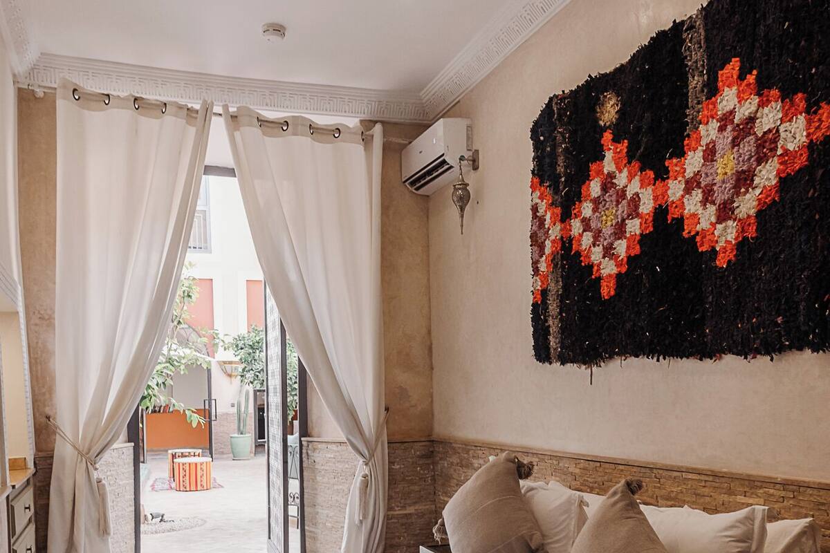 A bedroom with a bed, curtains, a wall-mounted light, and a decorative rug.