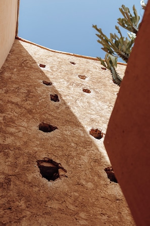 A view of a building's exterior with multiple holes in the wall, a clear blue sky, and a cactus plant in the foreground. - Le Riad Medina Privilège & Spa (Marrakech)