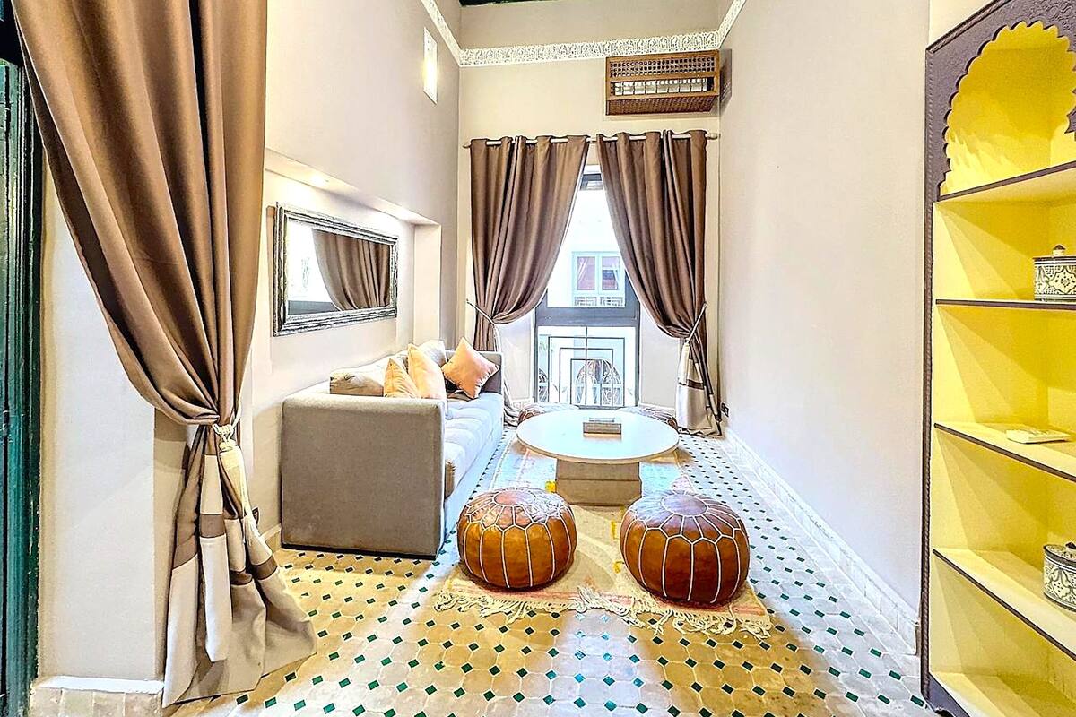 A cozy room with a sofa, ottomans, a small table, and a yellow shelf.