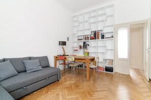 Un salon avec un canapé gris, une table à manger en bois avec des chaises, une bibliothèque blanche et une porte.
