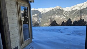 Una cabana de fusta amb una finestra que dona a un paisatge nevós i muntanyes.