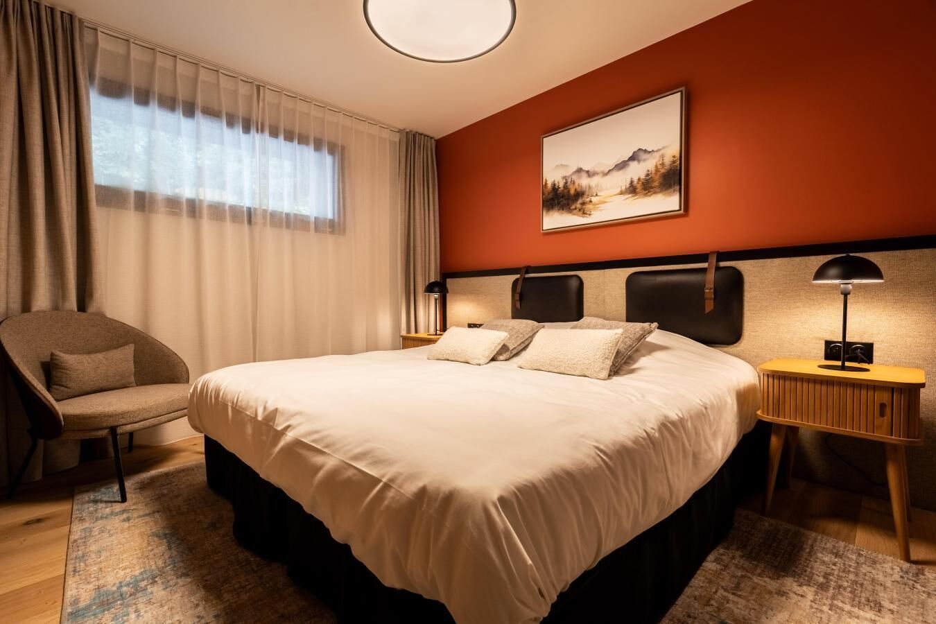 Una habitación de hotel con una cama grande, una silla, una mesita de noche y un cuadro en la pared.