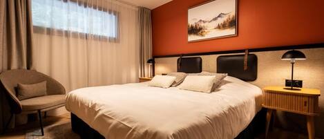 Una habitación de hotel con una cama grande, una silla, una mesita de noche y un cuadro en la pared.