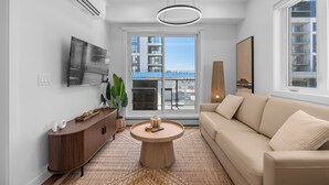Un salon moderne avec un canapé, une table basse, un téléviseur et une grande fenêtre donnant sur des immeubles.