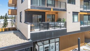 Un immeuble à plusieurs étages doté d’un balcon au deuxième étage, de grandes fenêtres et d’une zone au sol recouverte de gravier.