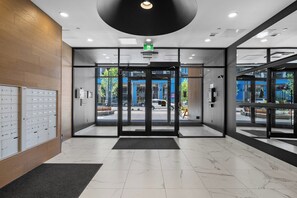 Een moderne hotellobby met een marmeren vloer, glazen deuren die naar de ingang leiden en een houten wand met een rij inbouwkastjes.