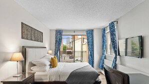 A modern bedroom with a bed, bedside table, lamp, and a TV on the wall. - Mural Oasis w Sunroom, Parking, near Stampede (Calgary)