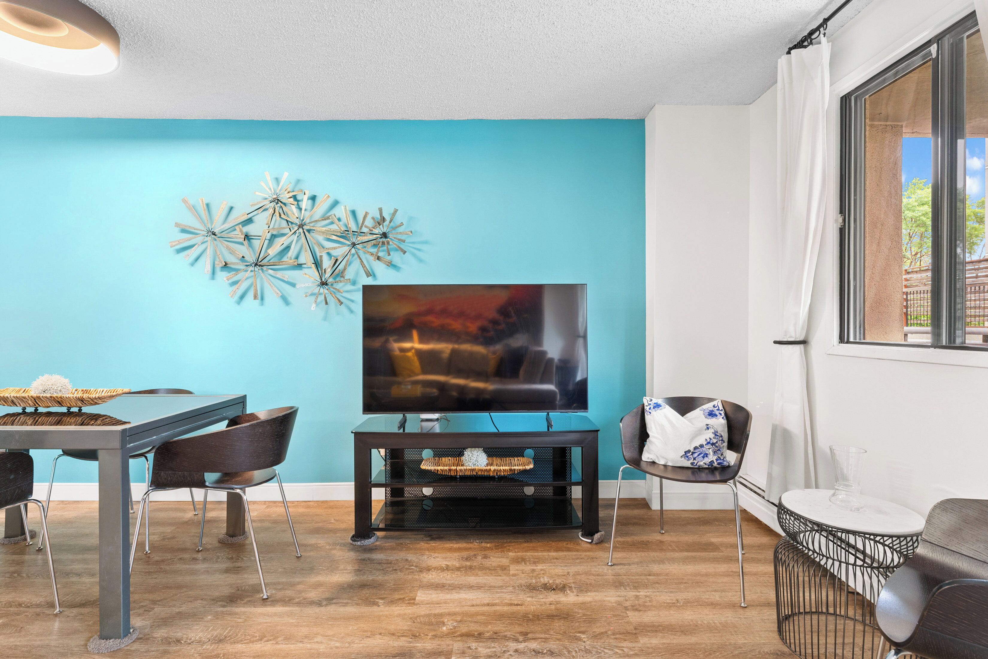 A modern living room with a blue wall, a flat-screen TV, a dining table with chairs, and a sofa.