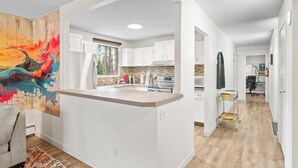 A modern kitchen with white cabinets, a large island, and a colorful abstract painting on the wall. - Mural Oasis w Sunroom, Parking, near Stampede (Calgary)