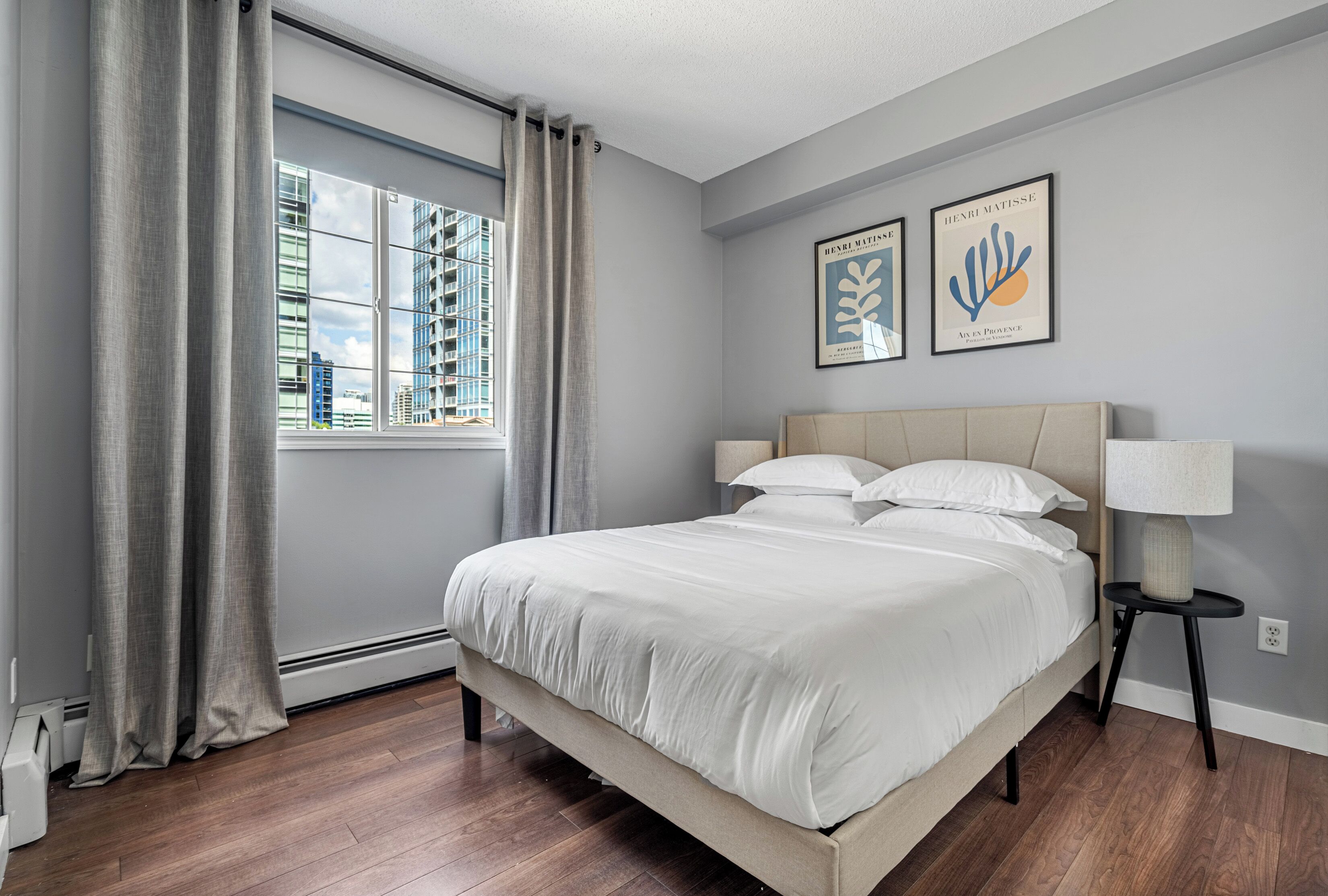 Un dormitorio moderno con una cama grande, una ventana con cortinas y dos cuadros en la pared.
