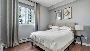 Un dormitorio moderno con una cama grande, una ventana con cortinas y dos cuadros en la pared.