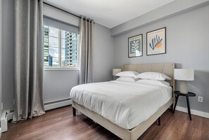 Ein modernes Schlafzimmer mit einem großen Bett, einem Fenster mit Vorhängen und zwei gerahmten Kunstwerken an der Wand.