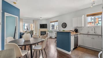 Una cocina moderna con armarios blancos, un comedor con mesa y sillas redondas, y una sala de estar con sofá y televisor.