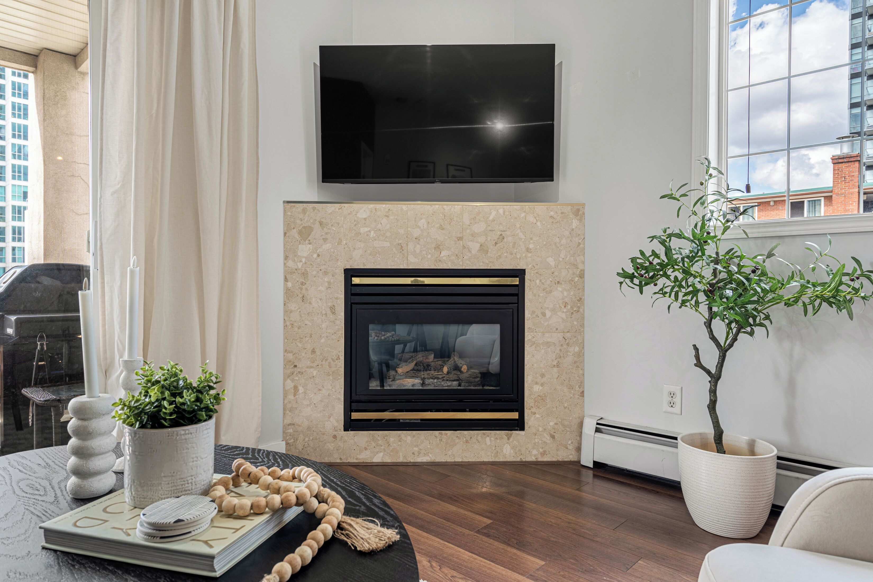 A modern living room with a fireplace, a flat-screen TV mounted above it, a potted plant, and a dining area with a table and chairs.
