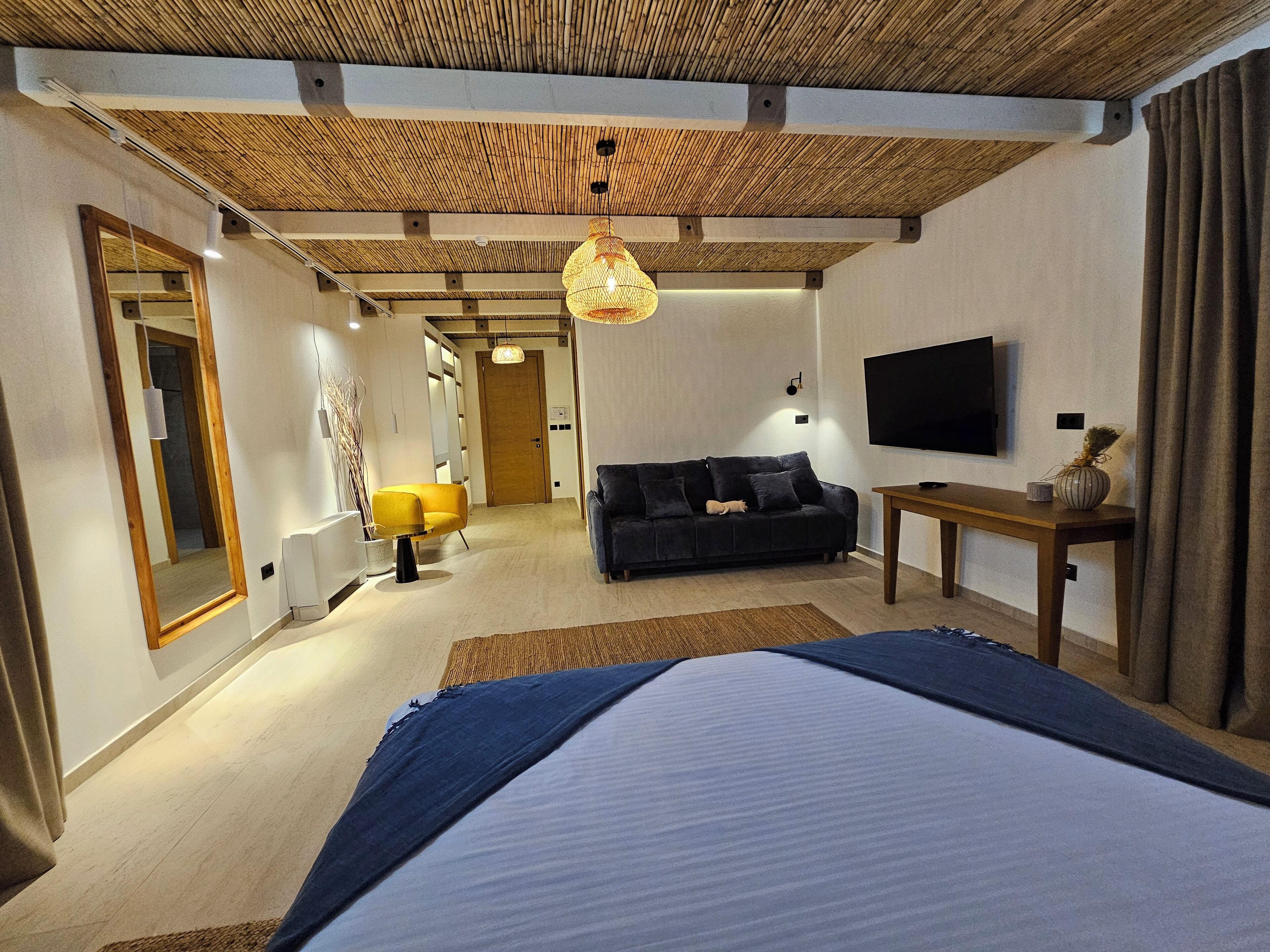 A modern bedroom with a large bed, a sofa, a TV, and a wooden ceiling.