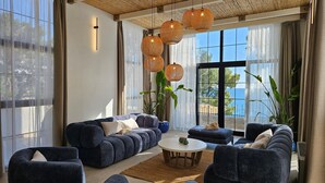 A modern living room with dark blue sofas, a round coffee table, and large windows with sheer curtains. - SeiSensi Luxury Beach Villa (Bar)