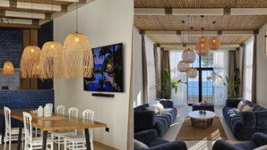 A modern living room with a large sofa set, a dining area with a wooden table and white chairs, and a large window with a view of the sea. - SeiSensi Luxury Beach Villa (Bar)