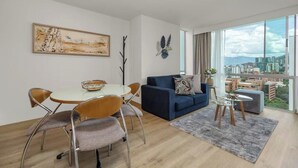 A modern living room with a dining area, a sofa, and a view of a cityscape through large windows.