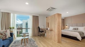 A modern hotel room with a large bed, a desk, a blue sofa, and a view of the city.