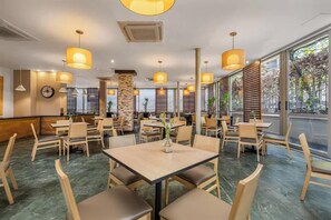 Un restaurant spacieux, doté de nombreuses tables et chaises, de grandes fenêtres et d’un éclairage suspendu.
