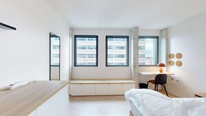 Una camera da letto moderna e minimalista con una scrivania integrata, un letto e ampie finestre con vista sulla città.