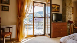 A hotel room with a large sliding glass door leading to a balcony, a wooden dresser with a flat-screen TV, and a chair.