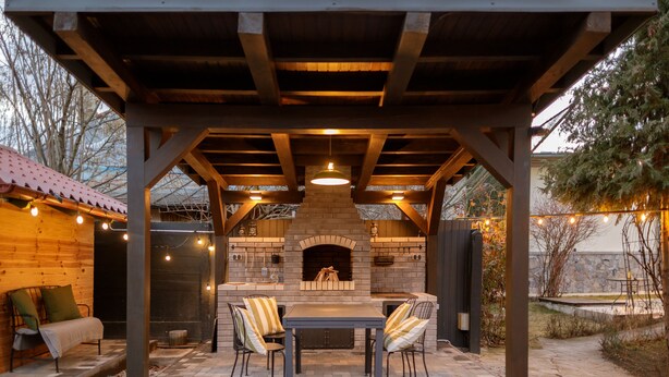 An outdoor patio with a brick fireplace, wooden pergola, and string lights. - Zaivan Retreat (Breaza de Jos)