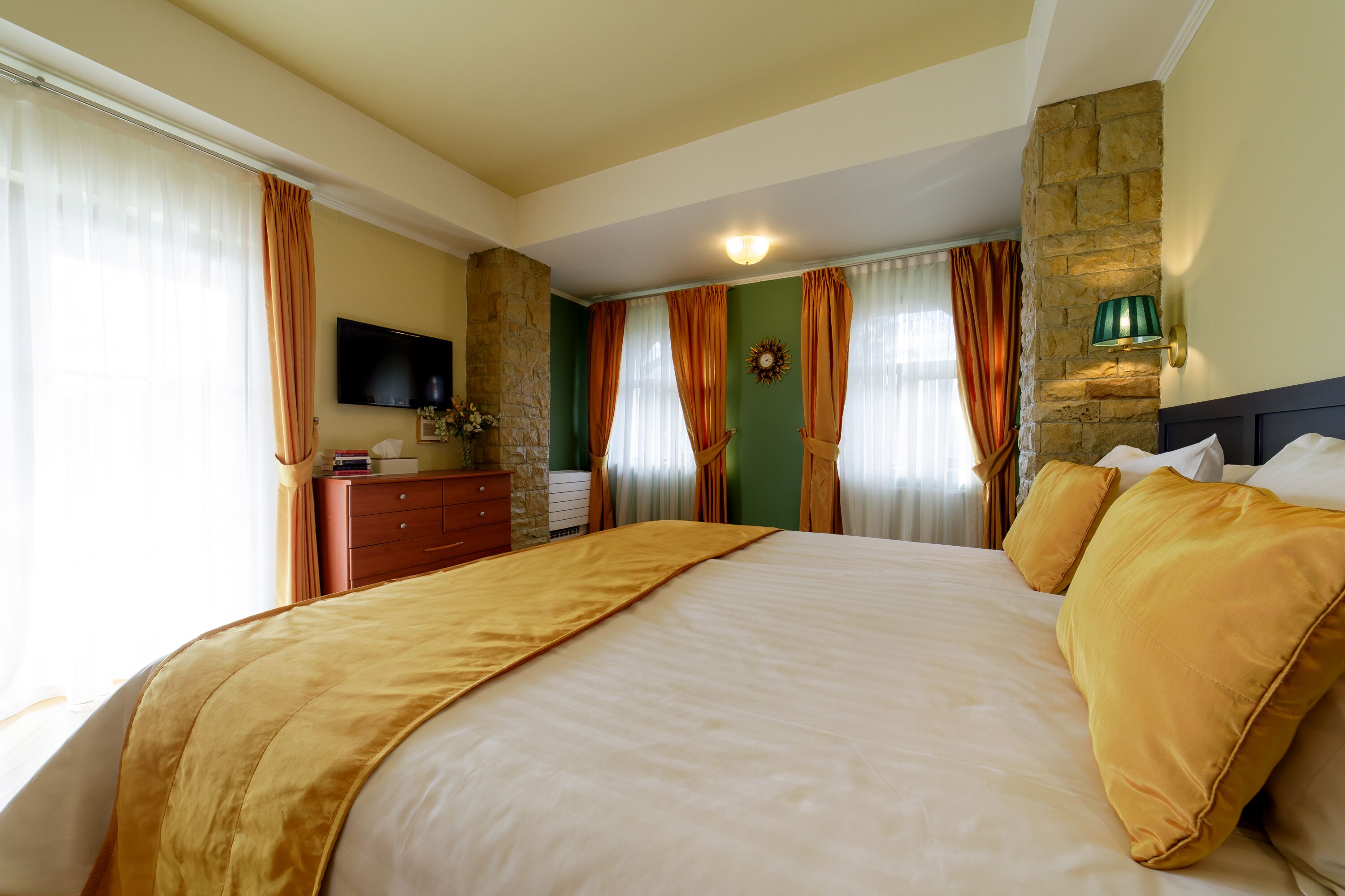 Una habitación de hotel con una cama grande, un aparador, un televisor de pantalla plana y una pared decorativa de piedra.