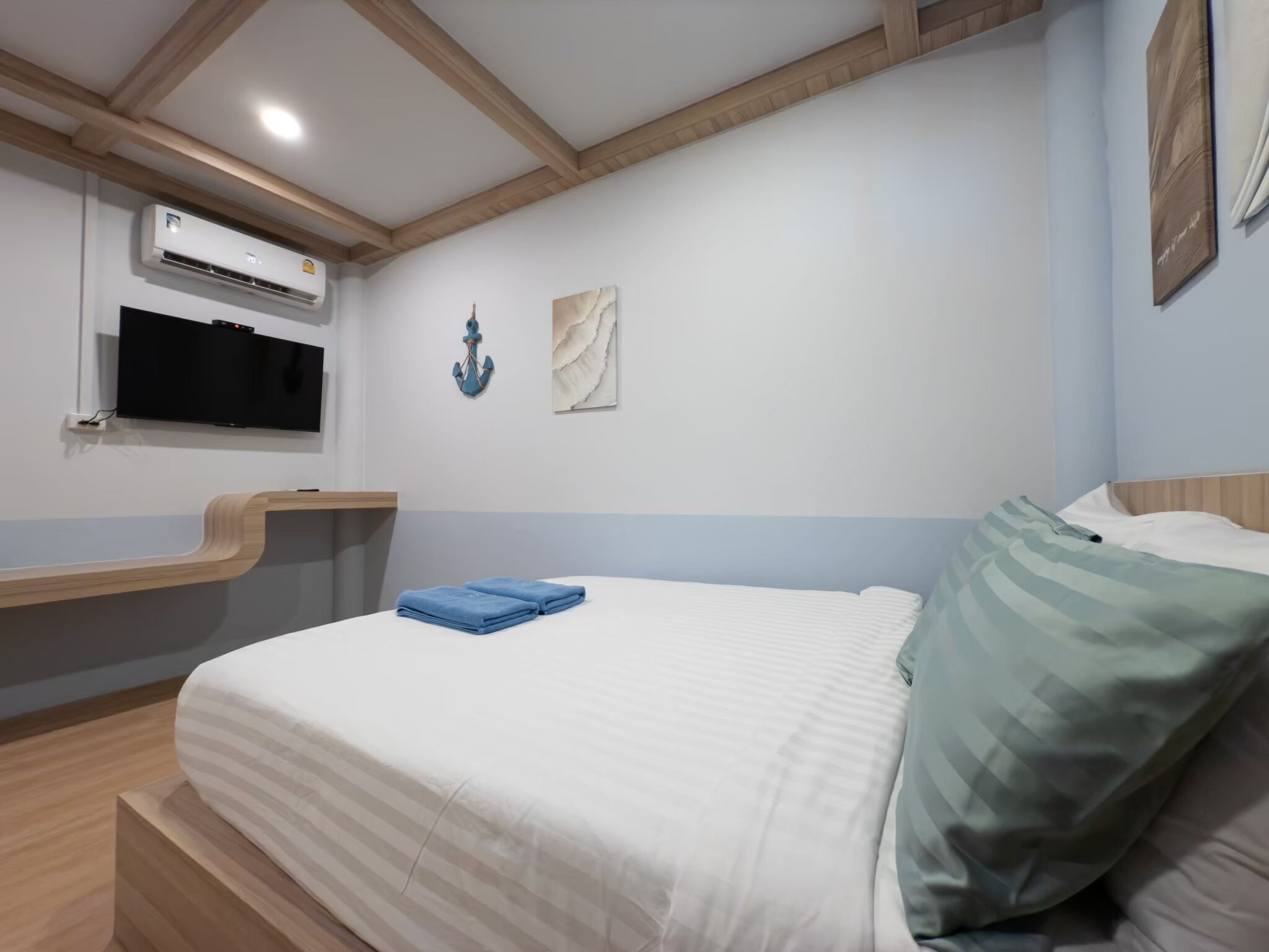A bedroom with a bed, a mounted TV, an air conditioning unit, and a wall-mounted artwork.