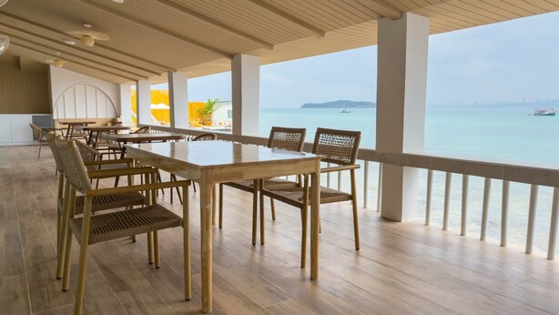 Un'ampia sala da pranzo con pavimento in legno e tavoli, affacciata su un mare tranquillo con imbarcazioni.