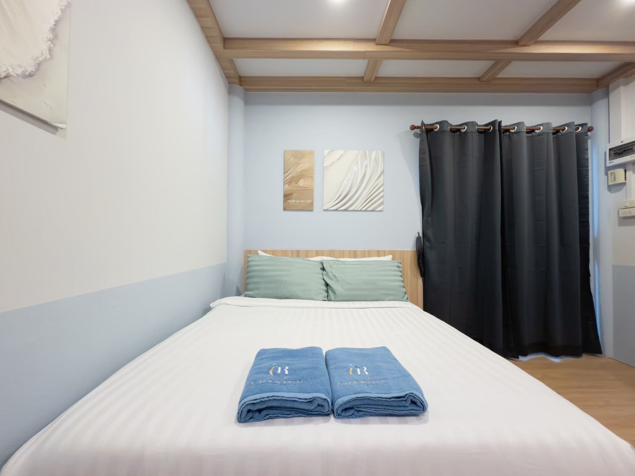A neatly made bed with two folded towels, a wooden headboard, and two wall art pieces.