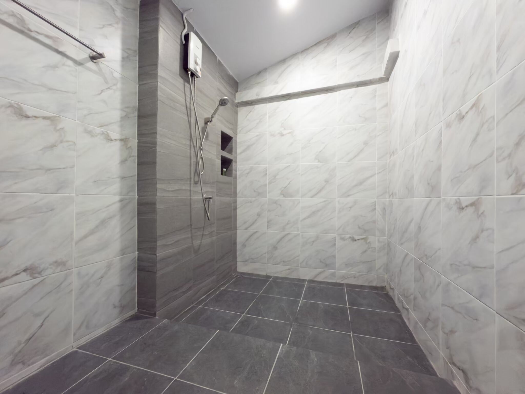 A modern bathroom with marble walls and dark tiles.