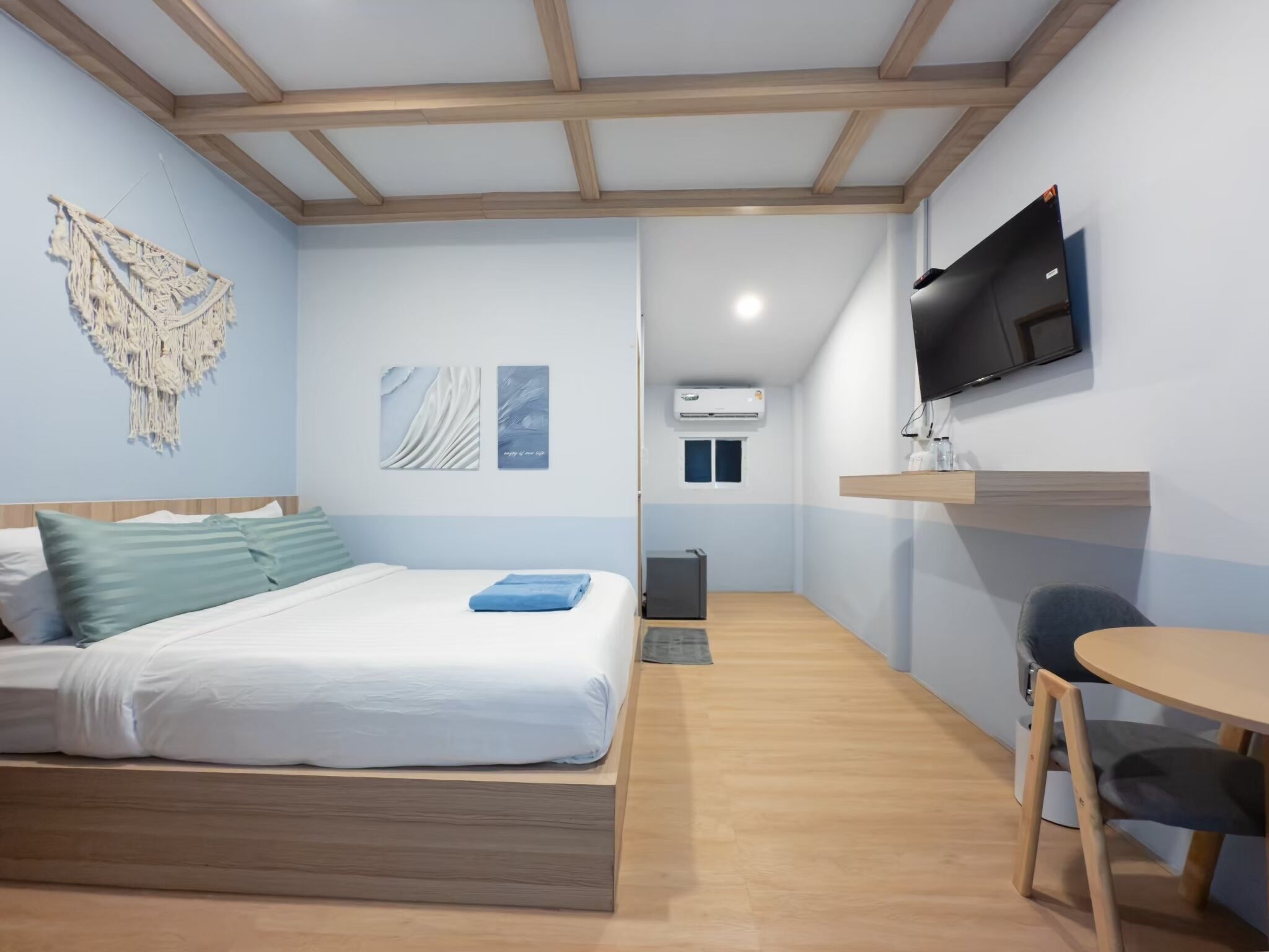 A bedroom with a bed, a desk, a chair, a television, and an air conditioning unit.