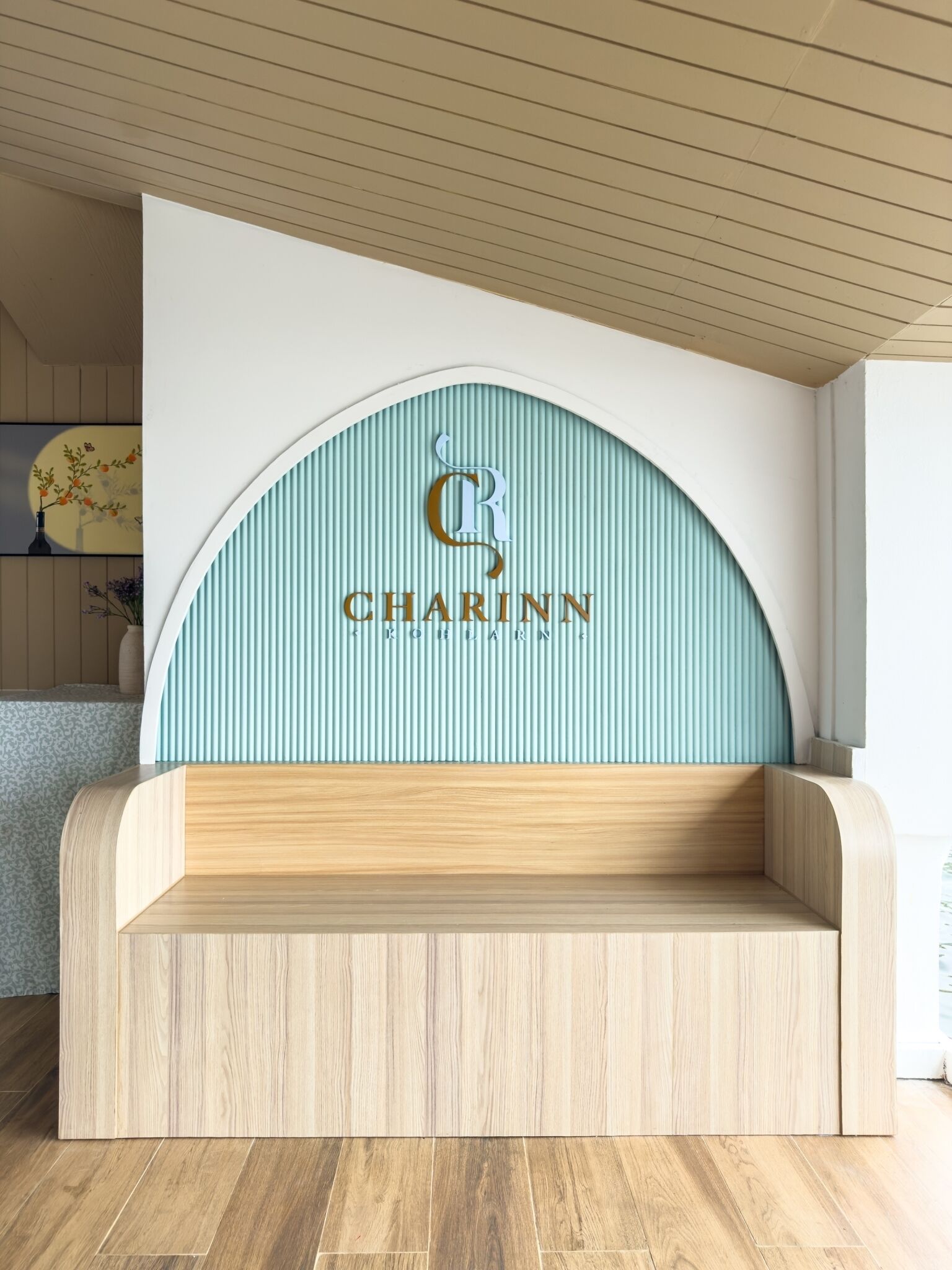 Um interior moderno com um banco de madeira curvo e um painel fixado na parede exibindo o logotipo e o nome 'CHARINN'.