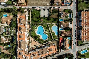 An aerial view of a residential area with two swimming pools, a road, and surrounding houses.