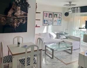A living room with a white sofa, a glass coffee table, a white dining table with chairs, and a chandelier. - Apartment 'Petunias Lorcrisur' with Sea View, Wi-Fi and Air Conditioning (Marbella)