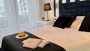Een netjes opgemaakt bed met een donkere hoofdeinde, een bedlampje en een hoed op het bed.