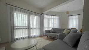 Una sala de estar moderna con un sofá gris, una mesa de centro redonda y cortinas de encaje.