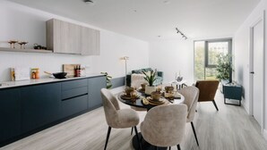 Una cocina moderna con armarios oscuros, un comedor con una mesa redonda y sillas, y un gran ventanal que ofrece vistas al exterior.