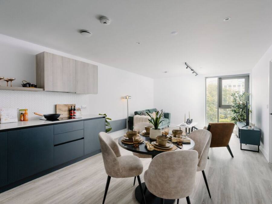 A modern kitchen with dark cabinets, a dining area with a round table and chairs, and a large window providing a view of the outdoors.