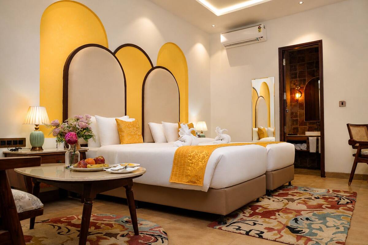 A hotel room with a large bed, a round table with a lamp, a chair, and a bathroom visible through an arched doorway.