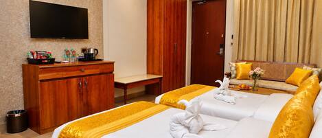 Ein Hotelzimmer mit Flachbildfernseher, Holzschrank, Schlafsofa mit gelb-weißer Bettwäsche und einem kleinen Tisch mit Blumenvase.