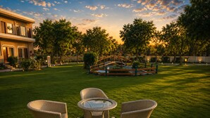 A well-maintained lawn with outdoor furniture, a small bridge, and a building in the background. - Kadamb Kuteer Vrindavan (Mathura)