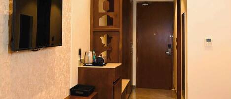 Ein Hotelgang mit einem an der Wand befestigten Fernseher, einem Holzbuchungsschalter, einem gemusterten Boden und einer Tür am Ende.