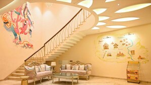 A spacious living area with a grand staircase, a sofa set, and a decorative wall map. - Kadamb Kuteer Vrindavan (Mathura)