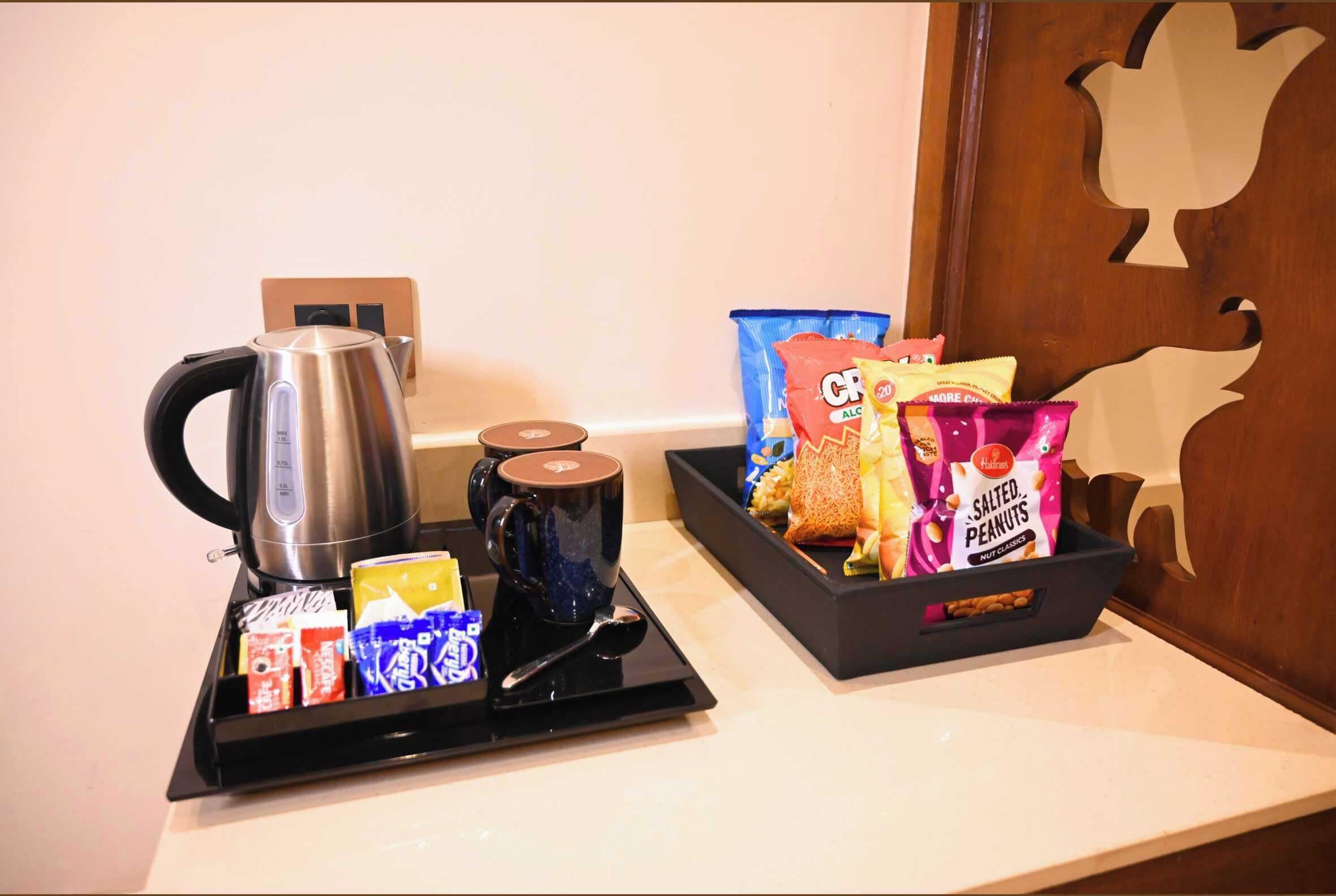 A tray with a kettle, a mug, and snacks including salted peanuts and chips.