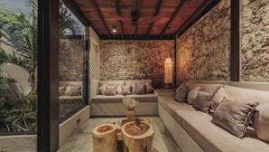 A cozy room with a stone wall, a wooden ceiling, and a large window. There are two sofas and a small table with a vase. - Casa del Espiritu Santo - La Santisima Cartagena (Unknown)