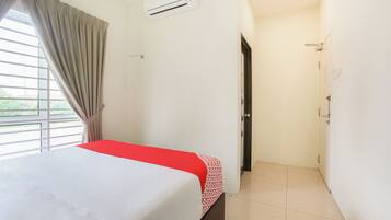 Une chambre d’hôtel comprenant un lit, une fenêtre avec des rideaux, un appareil de climatisation et une porte donnant accès à une salle de bain.