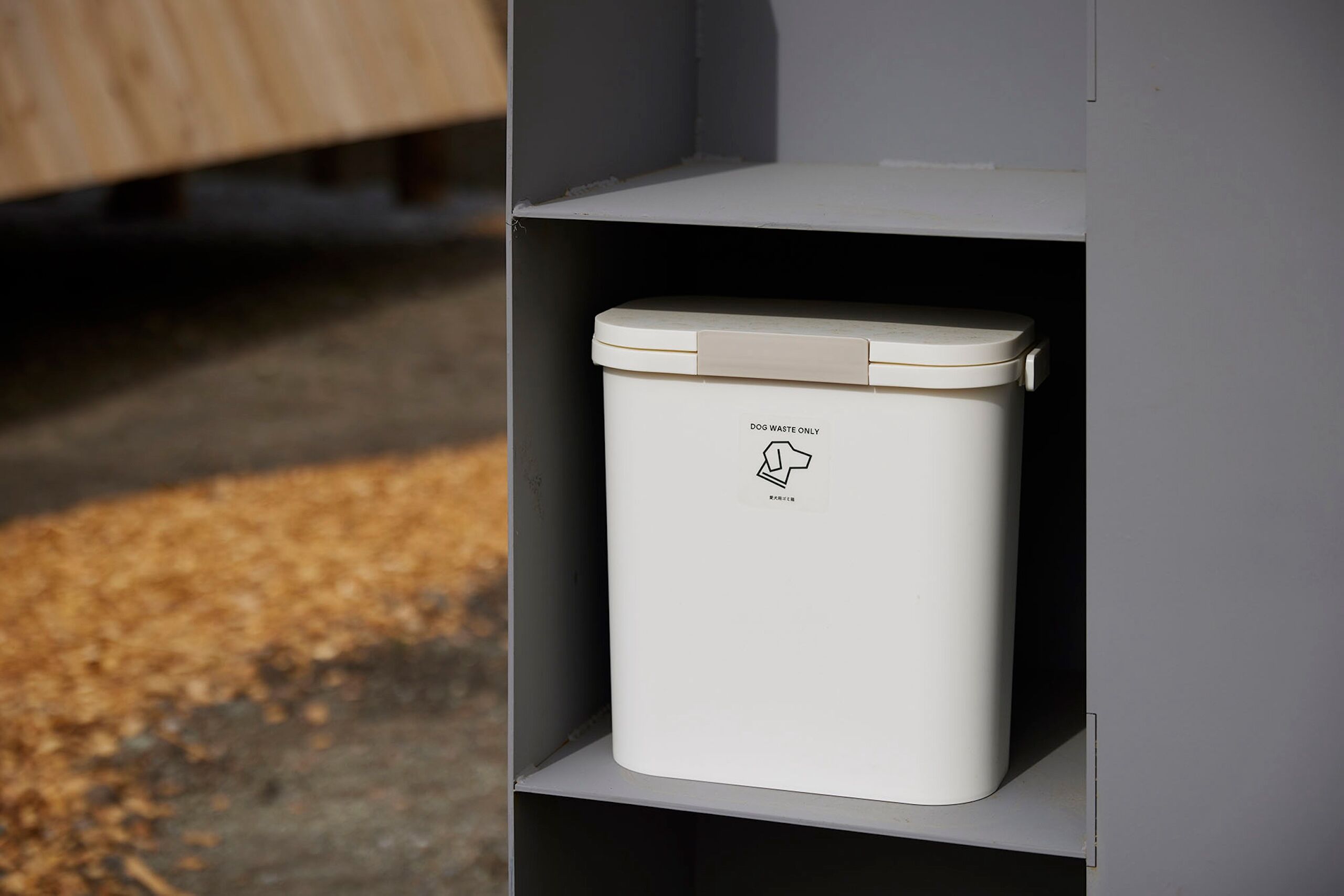 A white dog waste bin labeled "DOG WASTE ONLY" on a shelf.